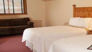 A hotel room with two single beds, a wooden headboard, bedside lamps, a nightstand, and a sofa. - Elkhorn Mountain Inn (Clancy)