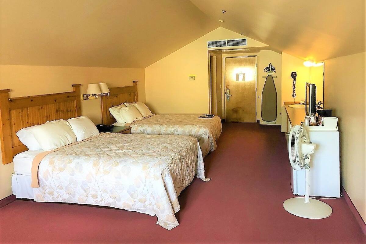 A hotel room with two beds, a desk, a chair, a mirror, a fan, and a door leading to a bathroom.