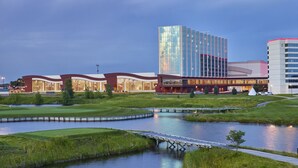 A modern hotel with a glass facade, a landscaped lawn, and a small bridge over a pond.