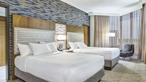 A hotel room with two beds, a large window with curtains, a chair, and a patterned carpet.