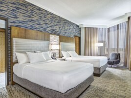 Habitación de hotel con dos camas, un ventanal con cortinas, una silla y alfombra estampada.