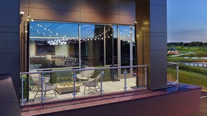 A modern building with a glass facade, outdoor seating area with wicker chairs, and a view of a golf course.