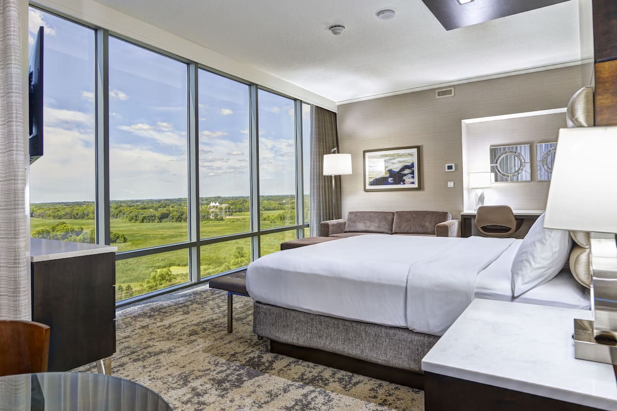 Ein Hotelzimmer mit einem großen Bett, einem Schreibtisch, einem Sessel und Blick ins Grüne.