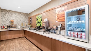 A breakfast bar with a refrigerator stocked with beverages, a coffee machine, and a display of pastries. - La Quinta Inn & Suites by Wyndham Logan (Logan)