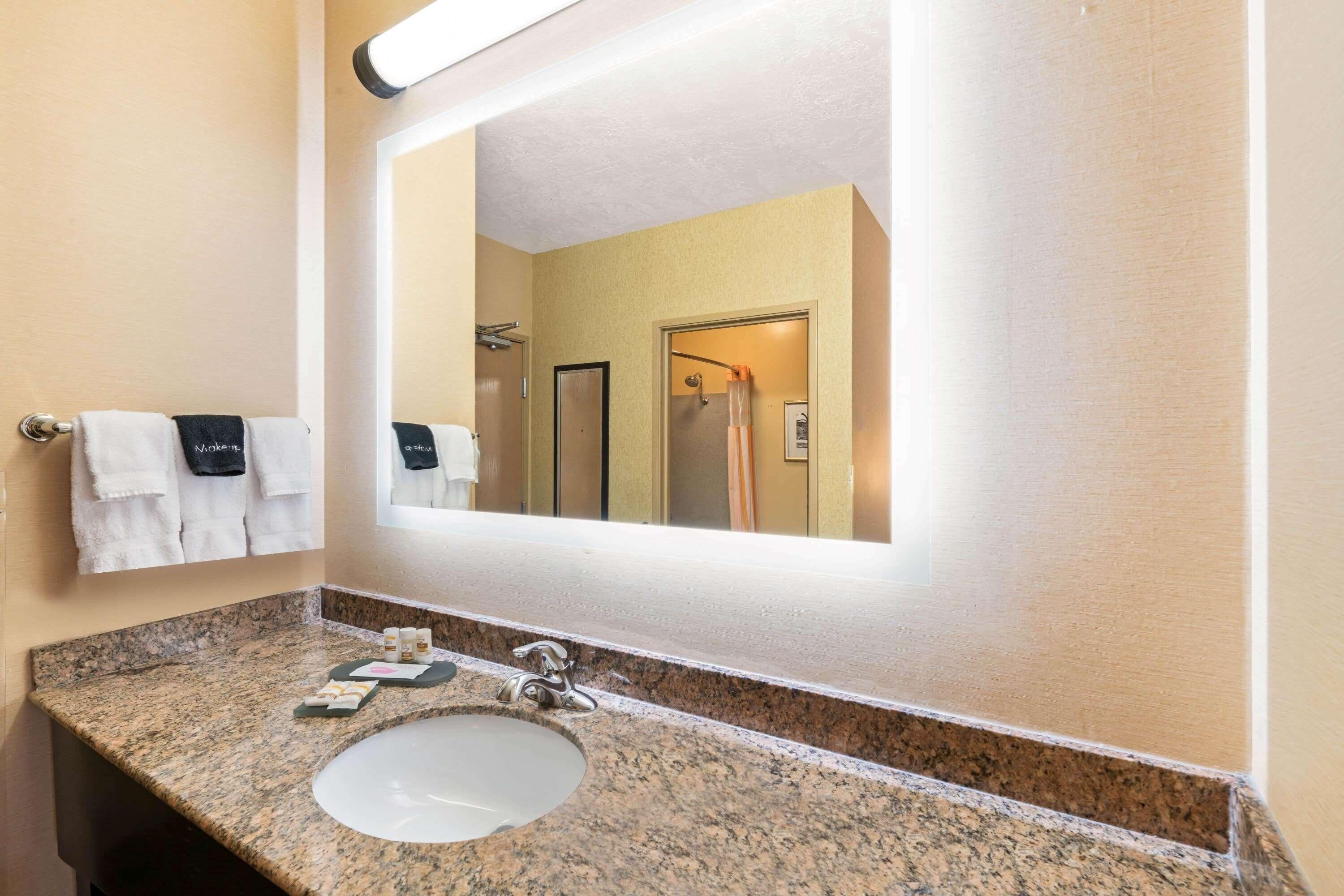 Un baño con encimera de granito, un lavabo blanco, un espejo grande y dos toallas colgadas en un perchero.