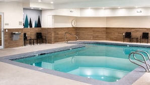 An indoor swimming pool with a tiled edge, a clock on the wall, and black chairs along the side. - La Quinta Inn & Suites by Wyndham Logan (Logan)