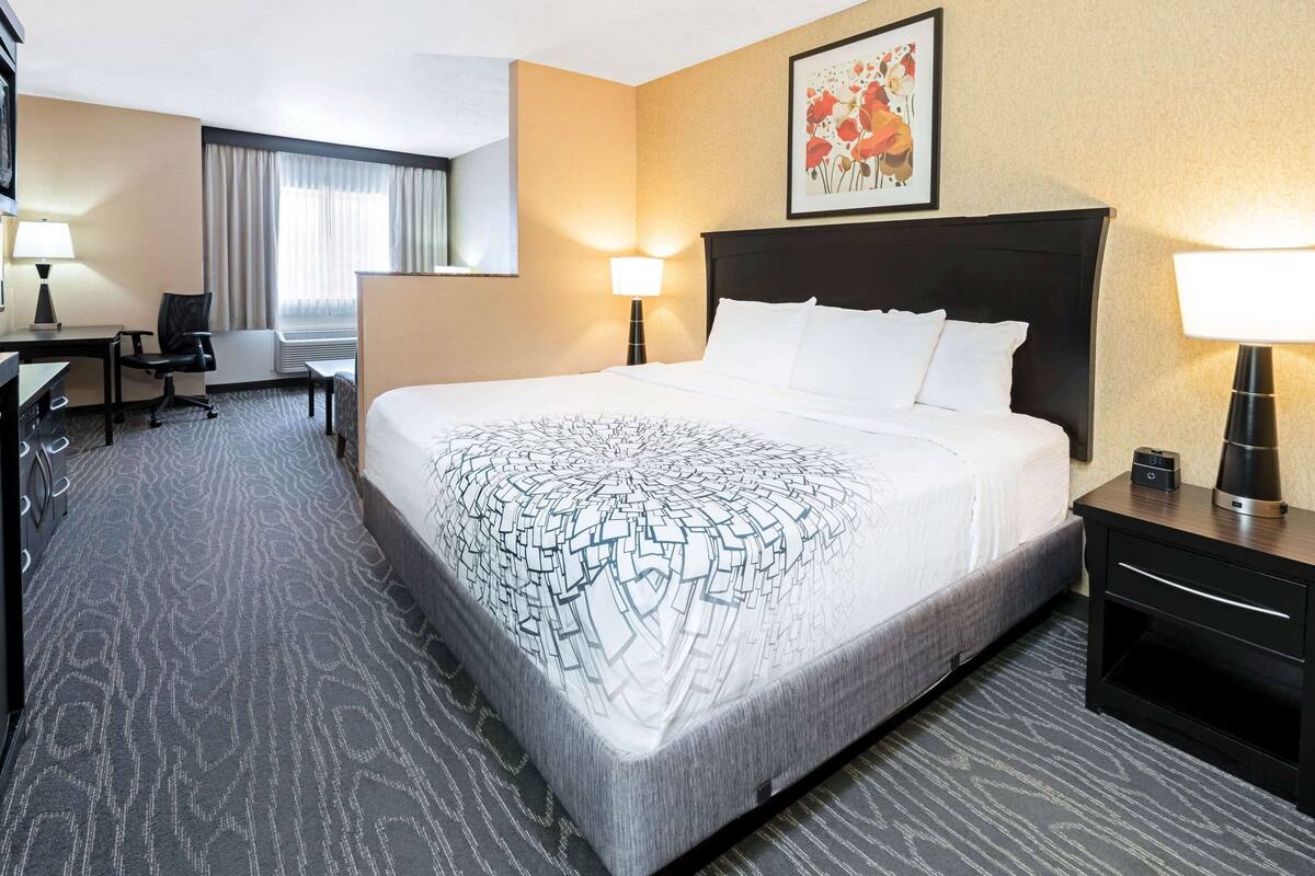 Ein Hotelzimmer mit einem großen Bett, einem Schreibtisch mit Stuhl, einer Lampe und einem Bild an der Wand.