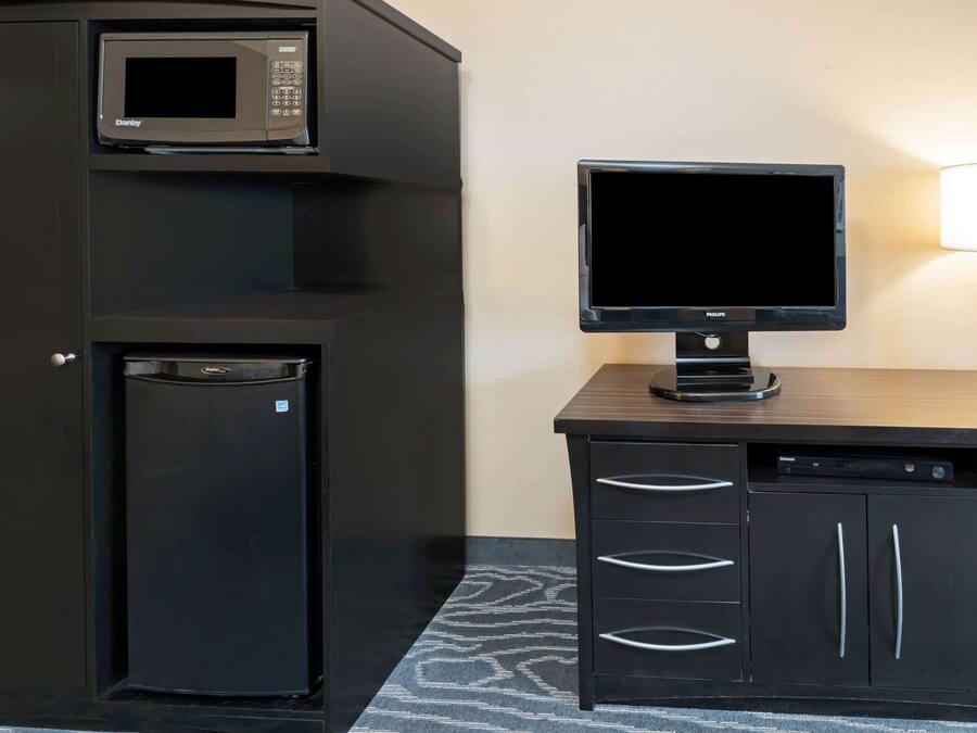 A compact kitchenette with a microwave, refrigerator, and a flat-screen TV on a wooden counter.