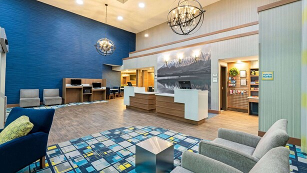 A modern lobby with a reception desk, seating area, and a large wall mural. - La Quinta Inn & Suites by Wyndham Logan (Logan)