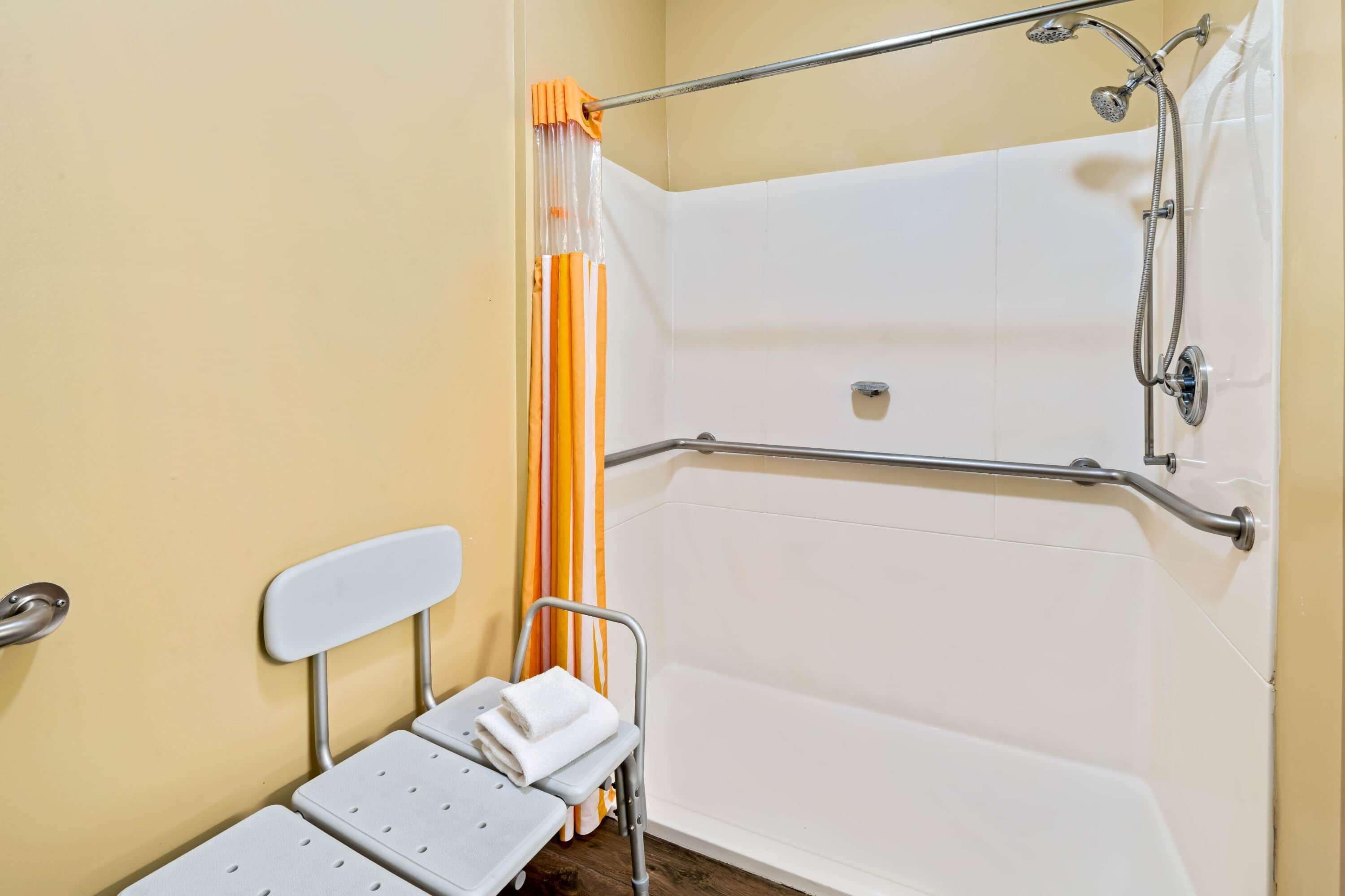 Une salle de bain équipée d’une douche, de barres d’appui, d’un banc accessible aux personnes en fauteuil roulant et d’un porte-serviettes.