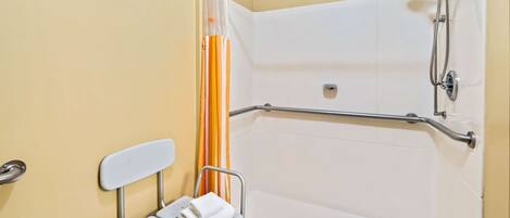 Une salle de bain équipée d’une douche, de barres d’appui, d’un banc accessible aux personnes en fauteuil roulant et d’un porte-serviettes.