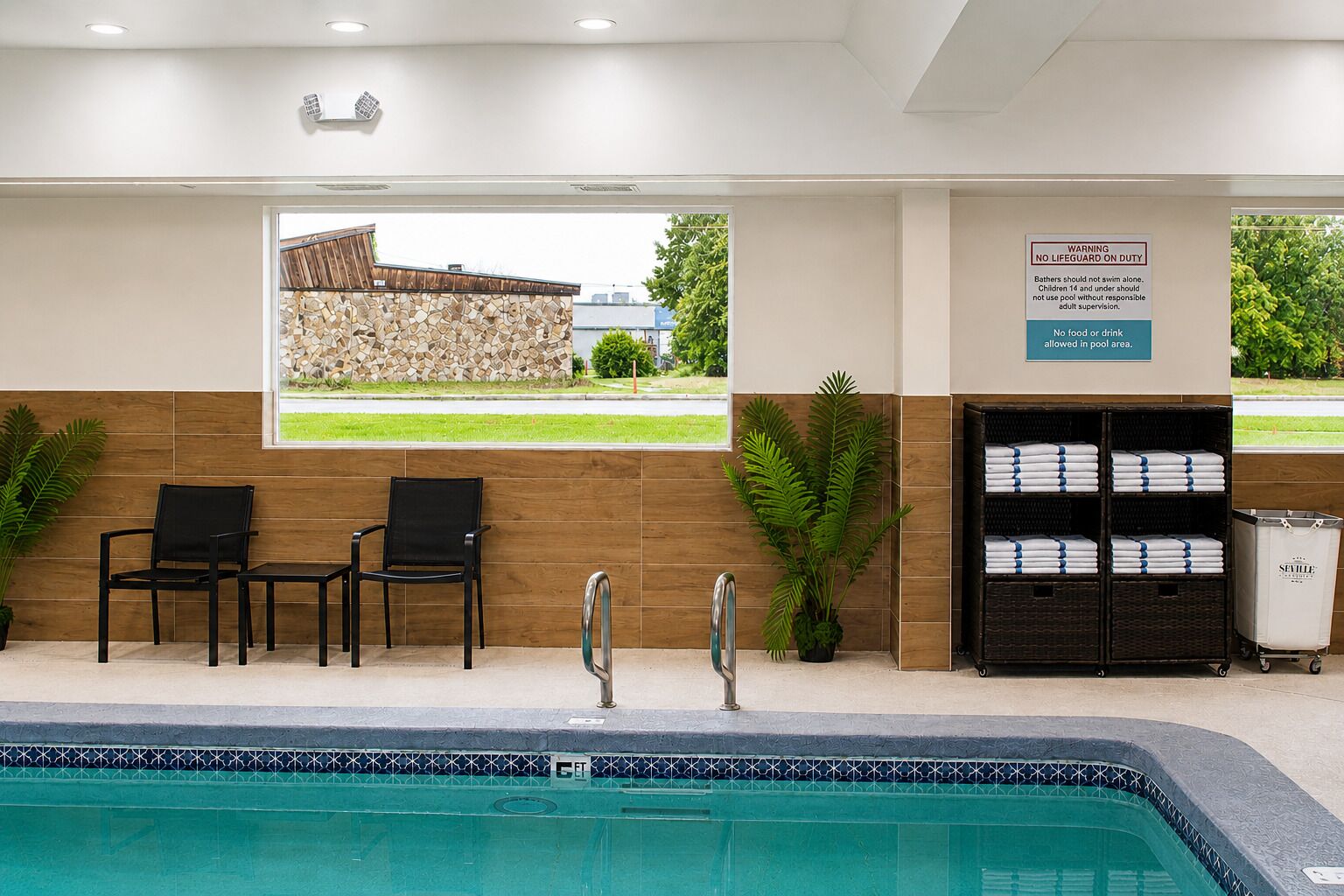 A pool area with chairs, a lifeguard sign, and a view of a stone wall and greenery.
