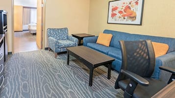 Habitación de hotel con sofá, sillón, mesa de centro y televisor.