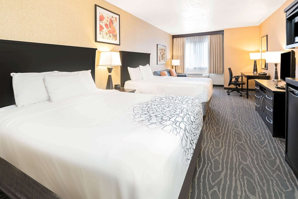Ein Hotelzimmer mit drei Betten, einem Schreibtisch, einem Sessel und einem Fernseher.