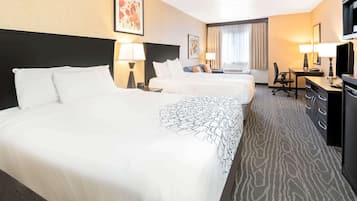 A hotel room with three beds, a desk, a chair, and a television.