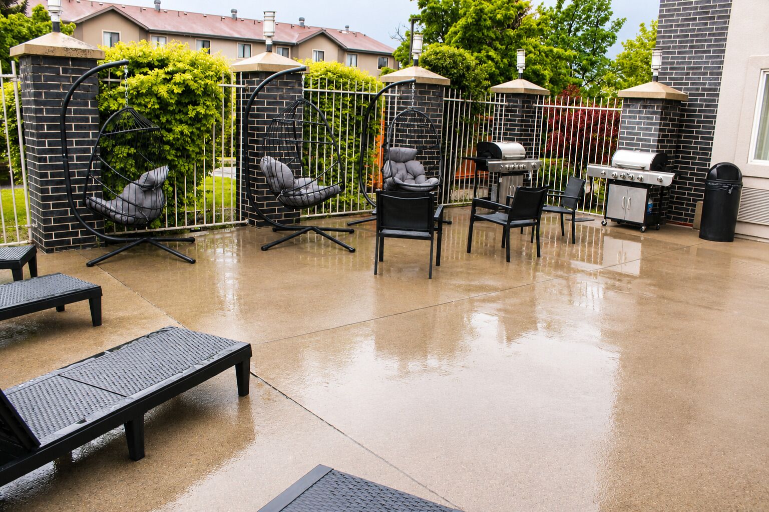 Un patio al aire libre con sillas de metal negro, una parrilla y un muro de ladrillo.