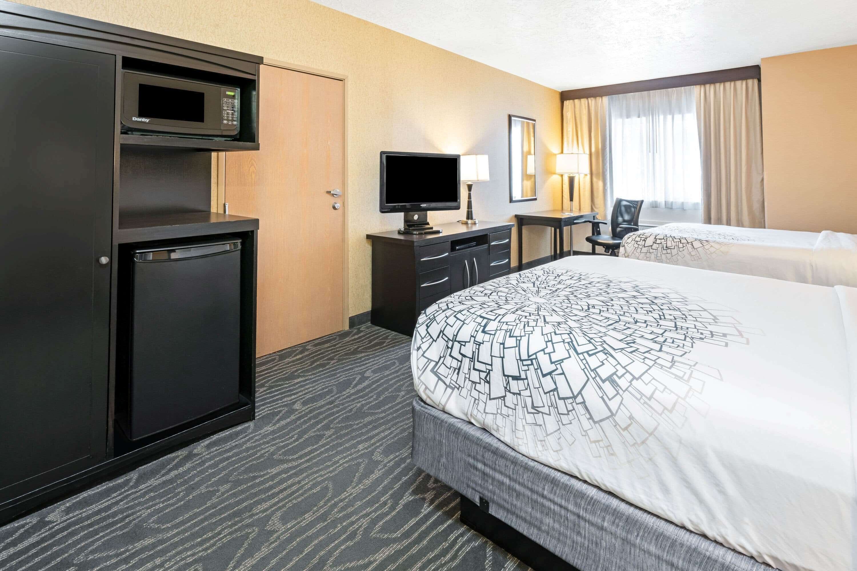 A hotel room with a bed, a desk with a computer, a television, and a minibar.