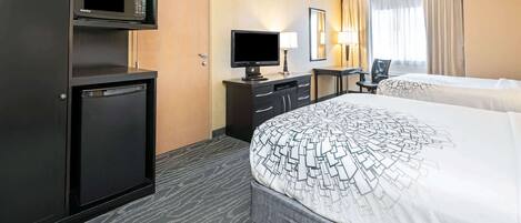 A hotel room with a bed, a desk with a computer, a television, and a minibar.