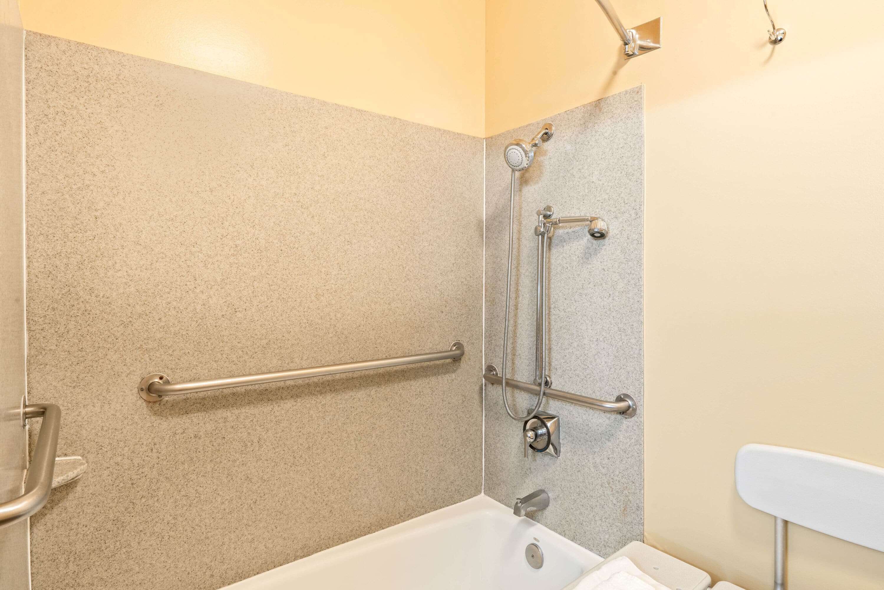 A bathroom with a bathtub, grab bars, and a shower head.