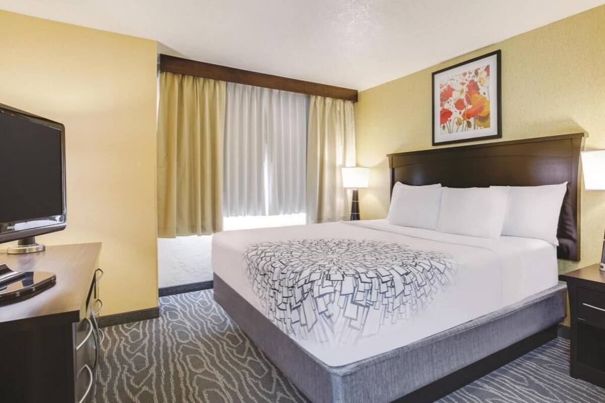 Ein Hotelzimmer mit Bett, Fernseher, Schreibtisch, Lampe und einem Gemälde an der Wand.
