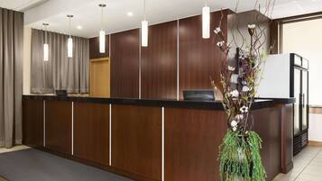 A reception area with a wooden reception desk, pendant lights, and a vase with branches and flowers.