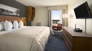 Habitación de hotel con una cama grande, un escritorio con teléfono, una silla, un televisor y una ventana con cortinas.