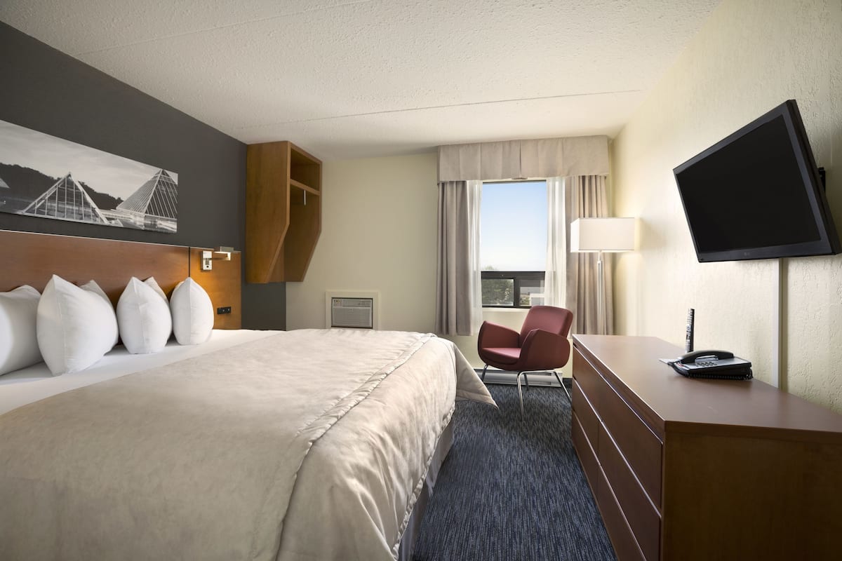 A hotel room with a large bed, a desk with a telephone, a chair, a television, and a window with curtains.