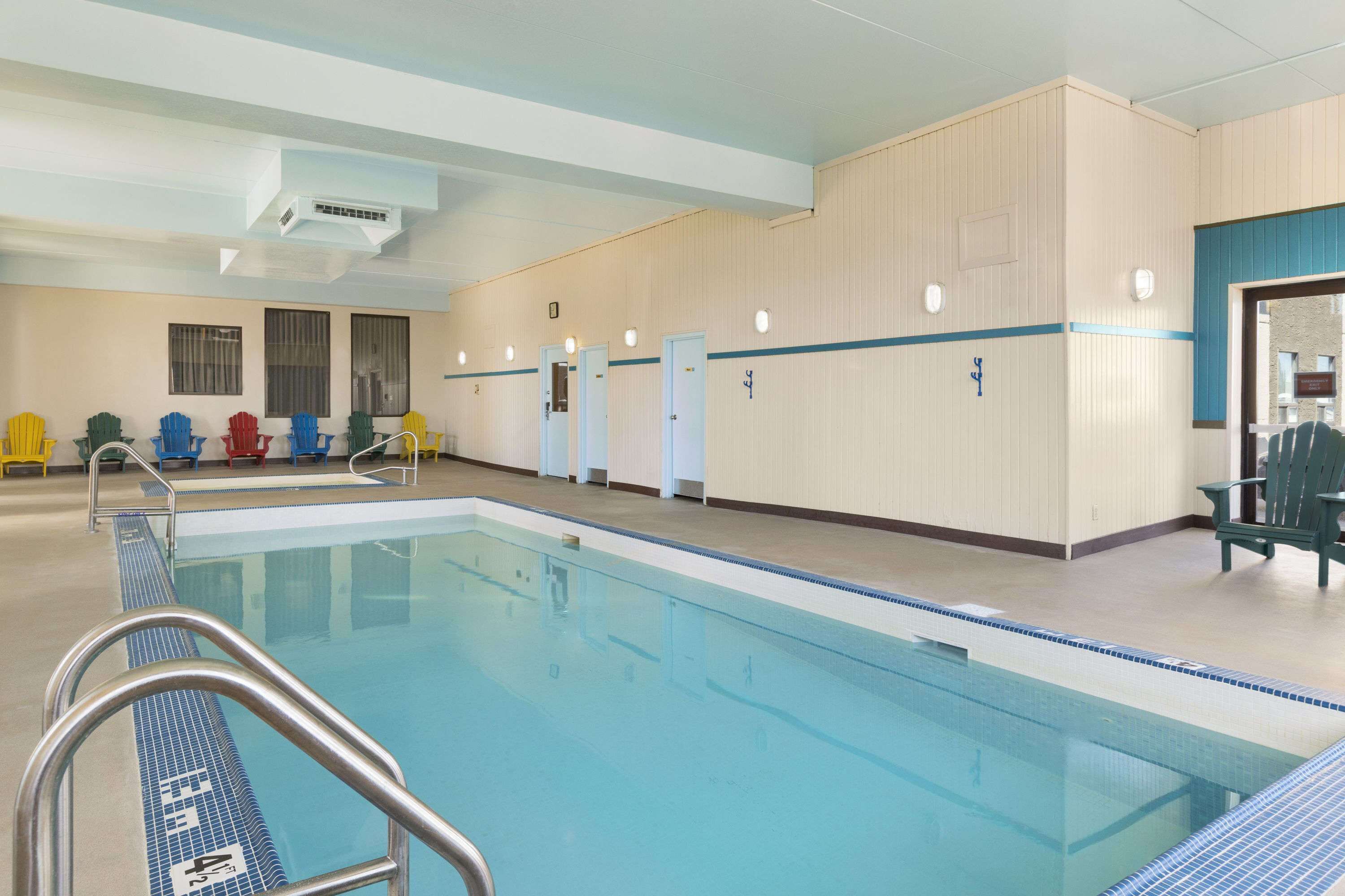 A swimming pool with a tiled deck and metal handrails. There are chairs and a door with a sign on the wall.