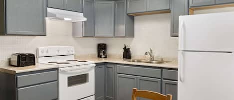 Una cocina con armarios grises, estufa blanca, fregadero y refrigerador.
