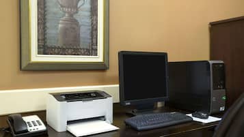 Un bureau avec un ordinateur de bureau, une imprimante, un téléphone et un tableau encadré accroché au mur.