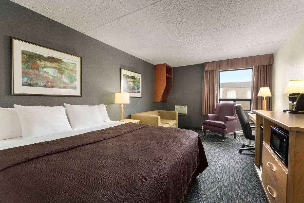 A hotel room with a large bed, a desk with a microwave, two chairs, and artwork on the walls.