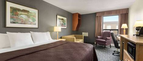 Ein Hotelzimmer mit einem großen Bett, einem Schreibtisch mit Mikrowelle, zwei Stühlen und Bildern an den Wänden.