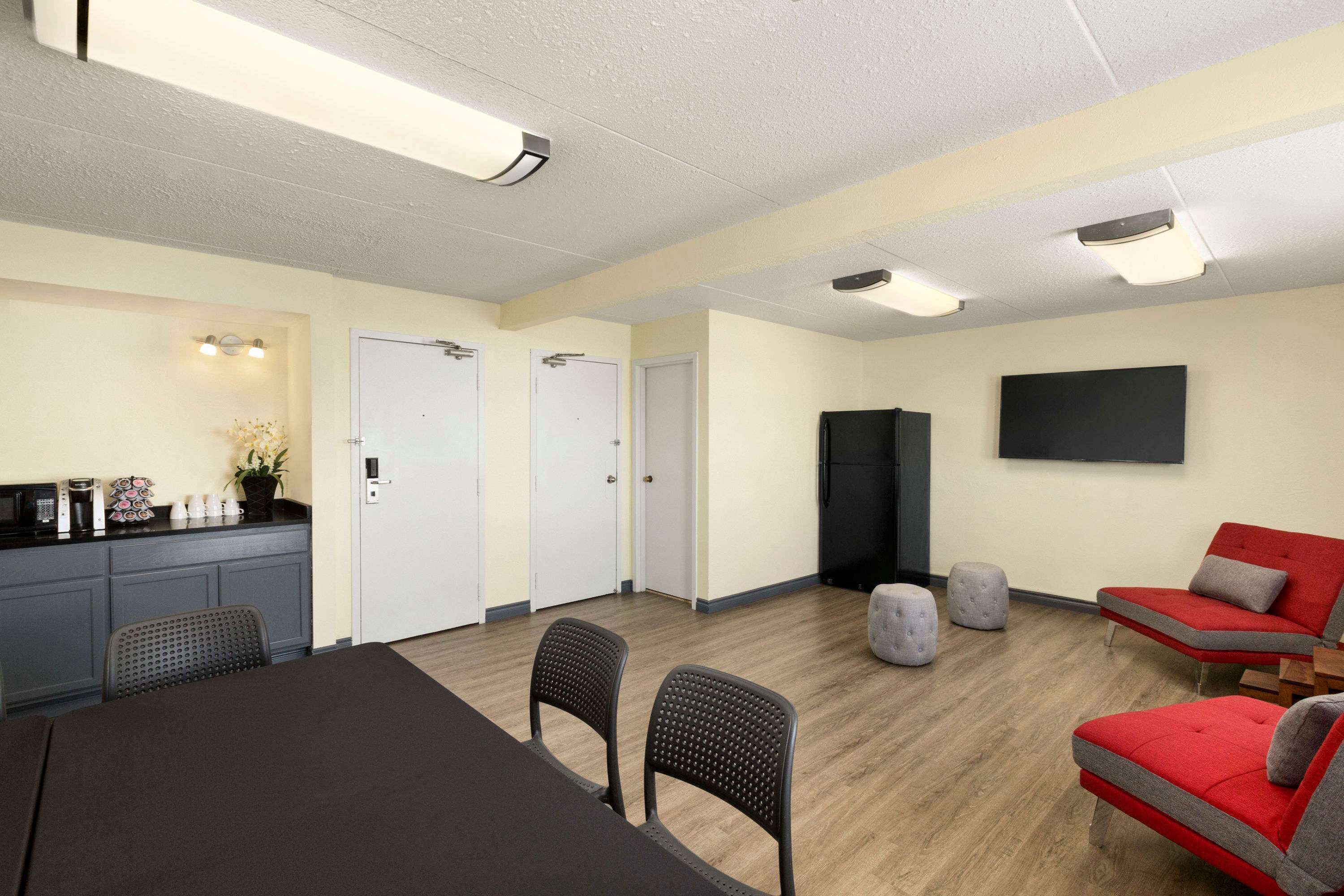 A conference room with a long table, two chairs, a red sofa, and a television on the wall.