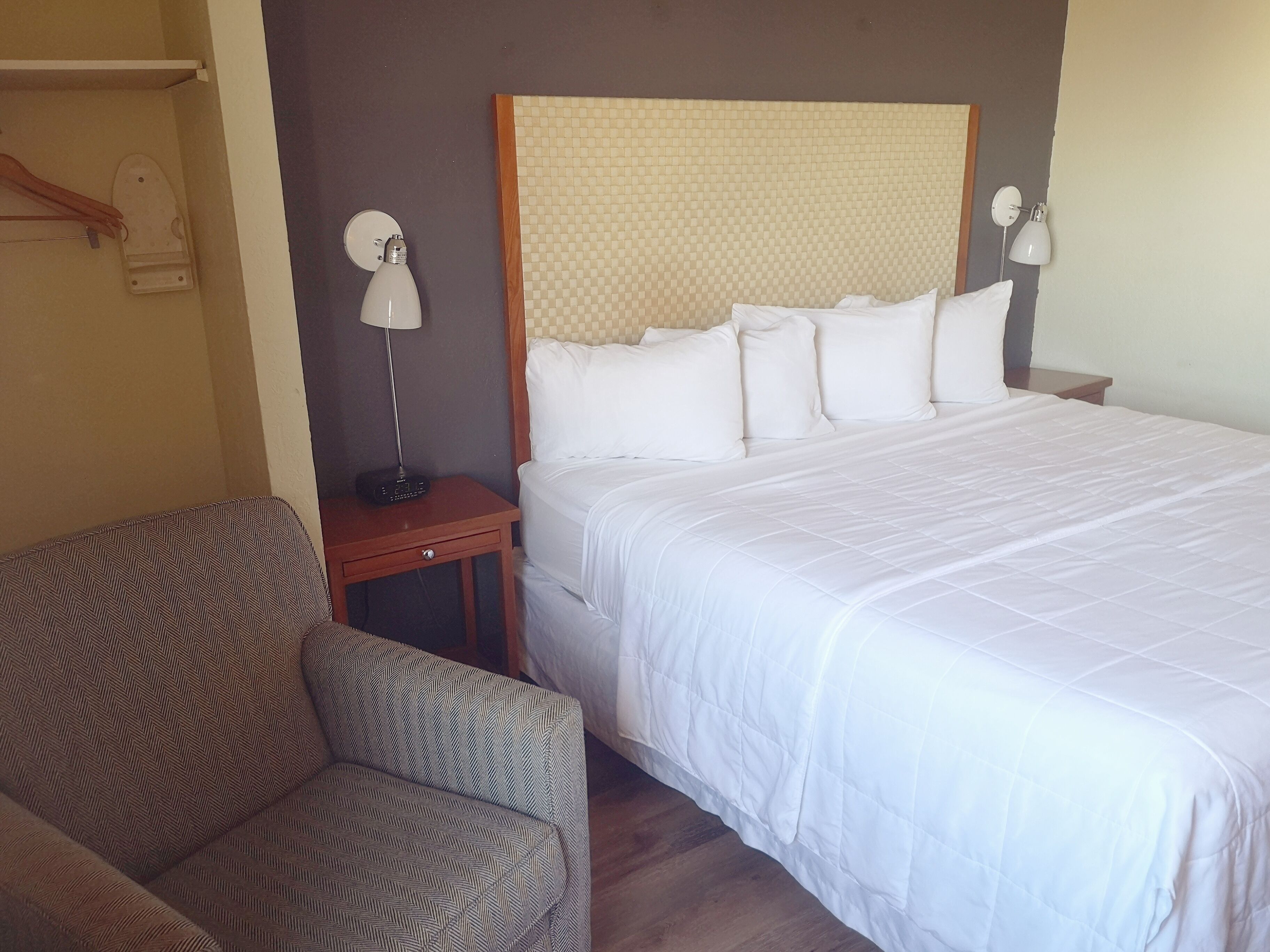 Una habitació d'hotel amb un llit gran, una tauleta de nit, una làmpada, una cadira i un armari.