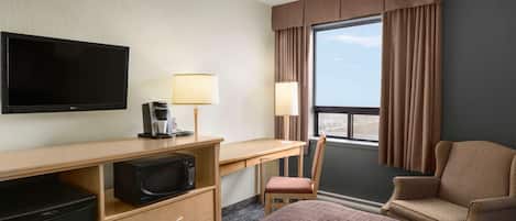 Quarto de hotel com cama, escrivaninha com computador, televisão, micro-ondas, cadeira e janela com cortinas.