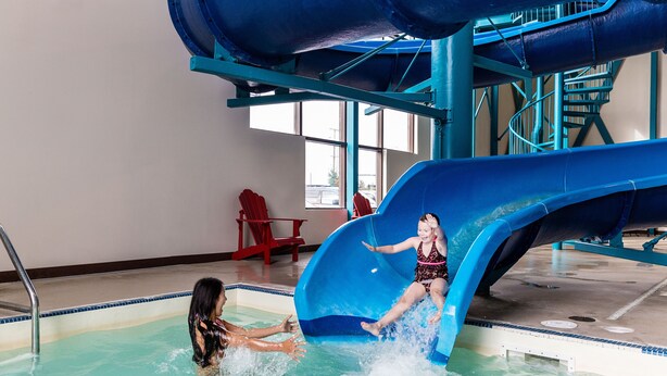 Tobogán acuático interior con zona de piscina, incluyendo una escalera para piscina y una silla roja al fondo.