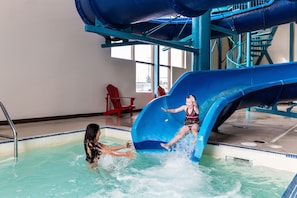 An indoor water slide with a pool area, including a pool ladder and a red chair in the background.