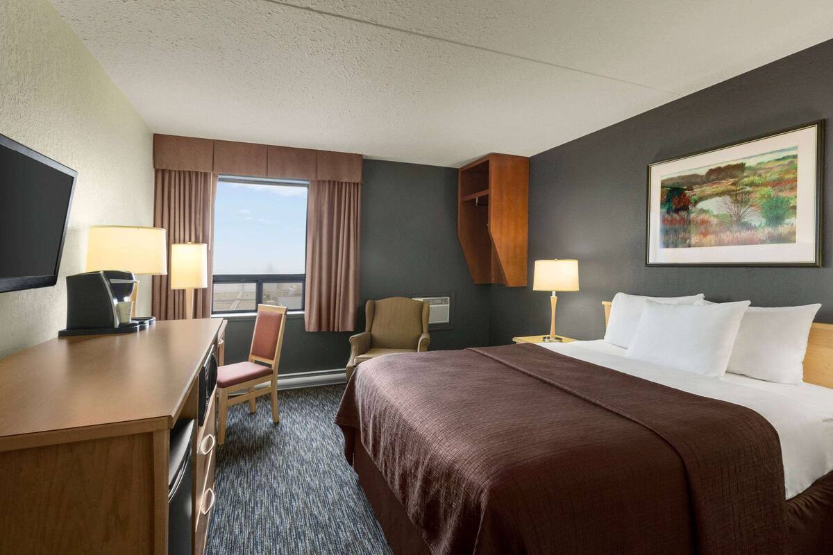 A hotel room with a large bed, a desk with a computer, a chair, two lamps, and a window with curtains.