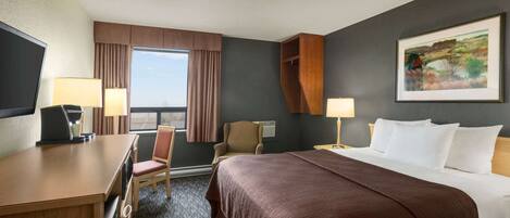 A hotel room with a large bed, a desk with a computer, a chair, two lamps, and a window with curtains.