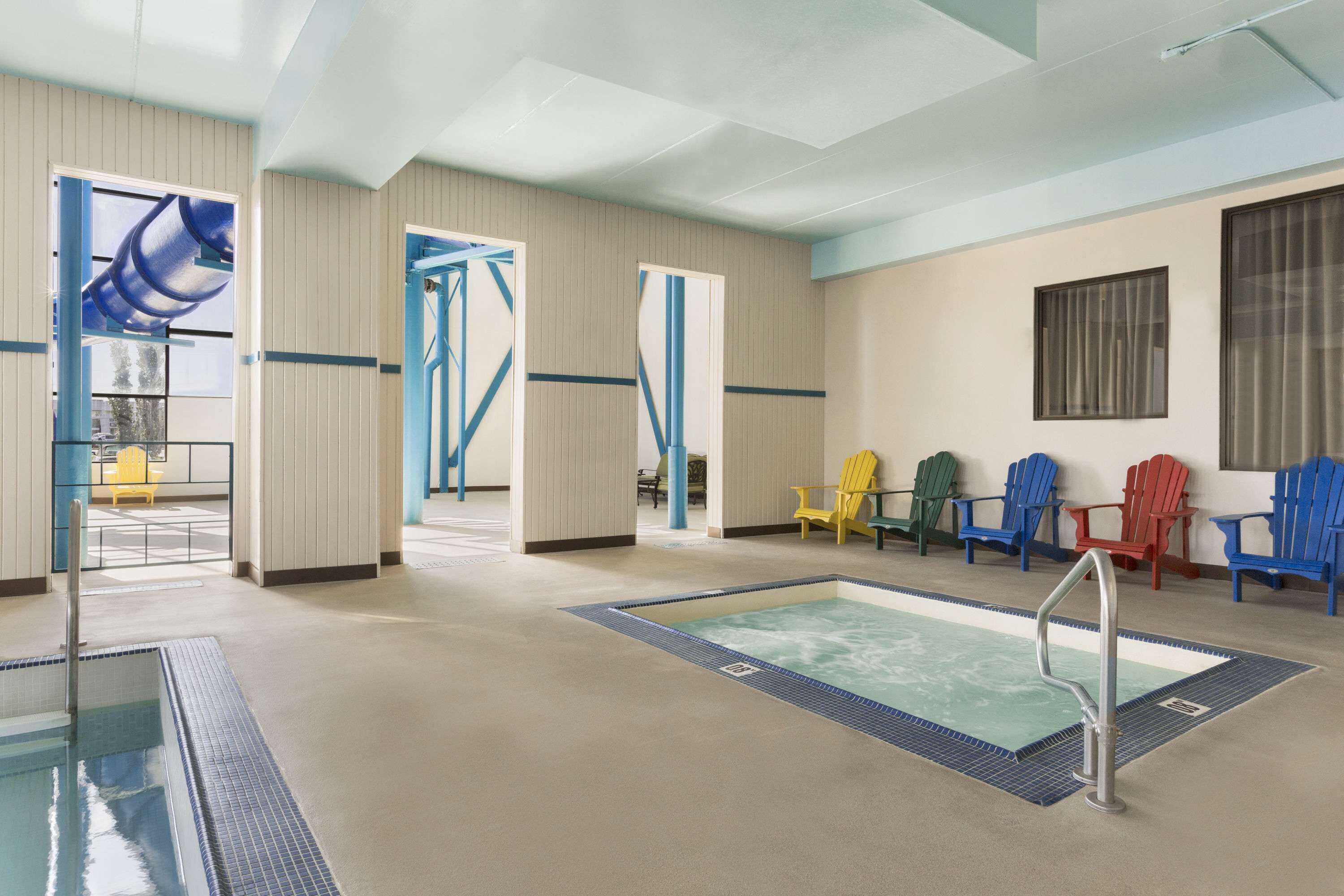 An indoor swimming pool area with a pool, a changing room, and several Adirondack chairs.