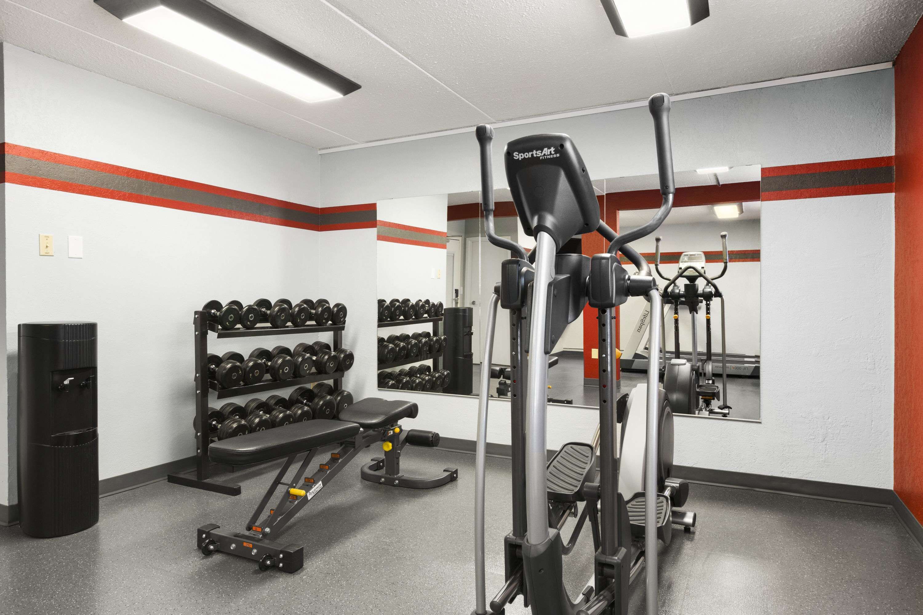 A gym with exercise equipment, a bench, and a rack of dumbbells.