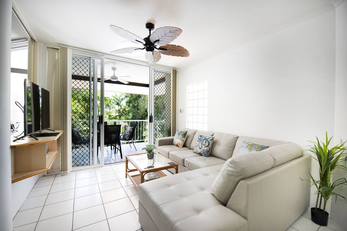 A modern living room with a sofa, coffee table, TV, and a ceiling fan.