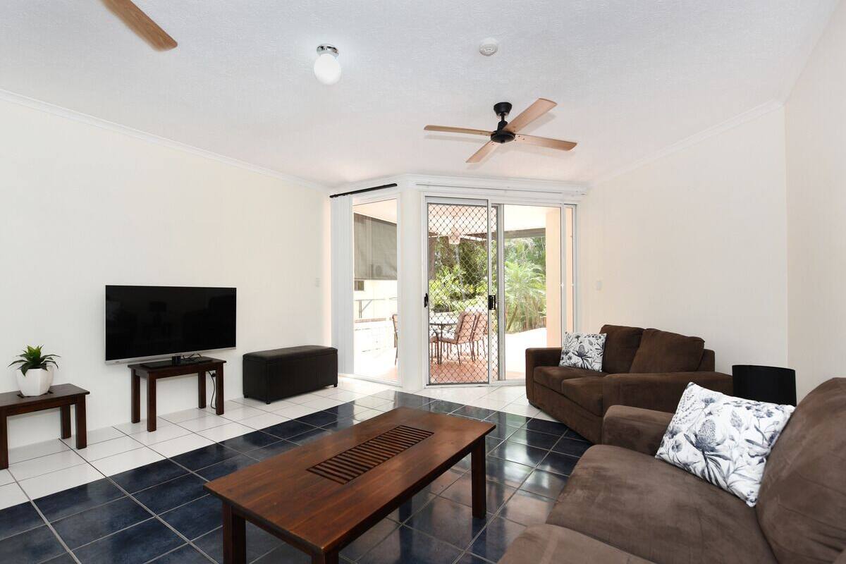 A living room with a flat-screen TV, a ceiling fan, a coffee table, and a sofa with floral cushions.
