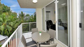 A balcony with a round table and chairs, a sliding glass door, and a view of palm trees.