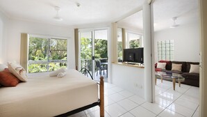 Una habitación amplia con cama, sofá, televisión y balcón con vistas a zonas verdes.