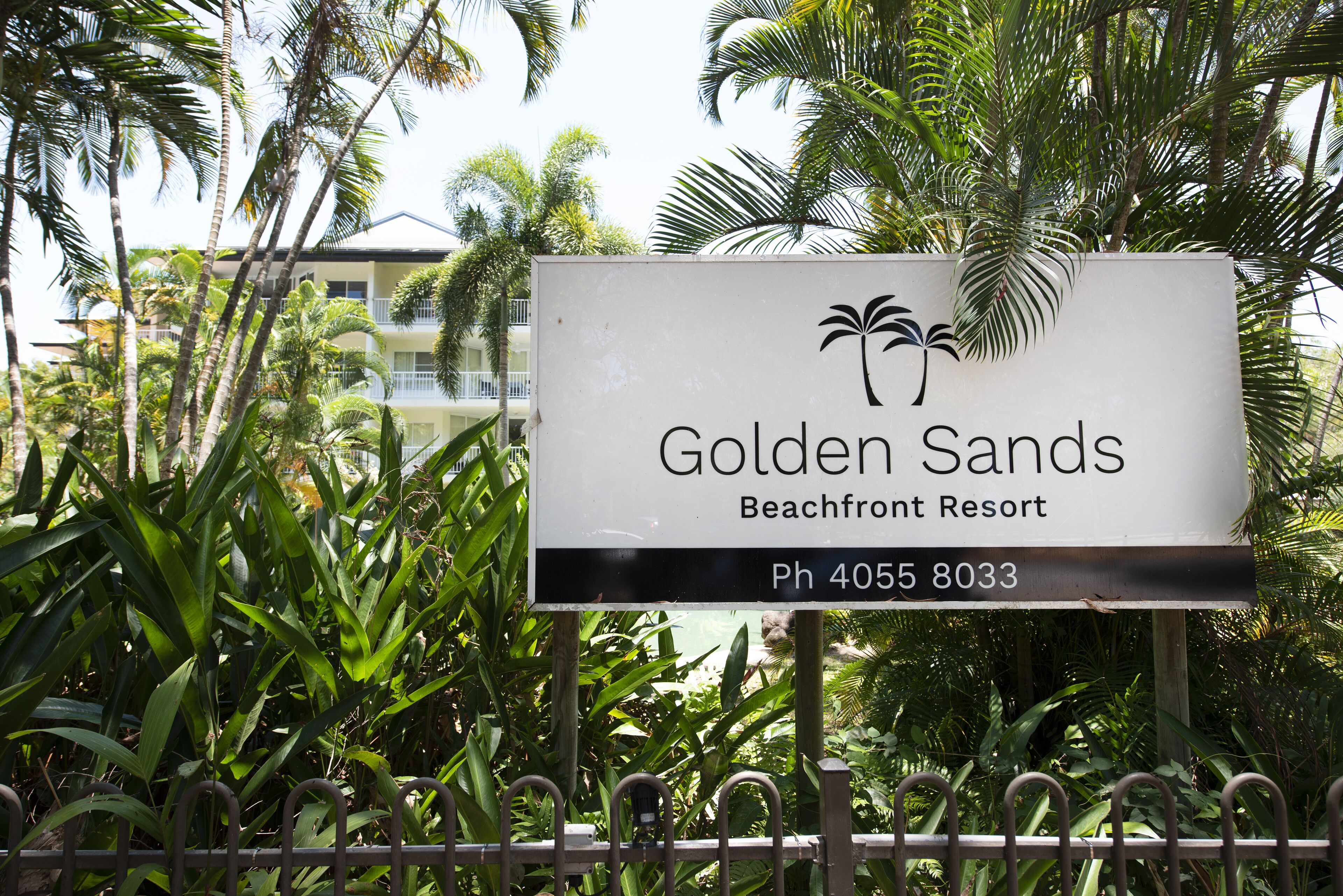 A sign for Golden Sands Beachfront Resort with a palm tree logo and contact number.