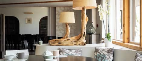 A modern lounge area with a round table, a sofa with floral cushions, and a unique wooden lamp stand.