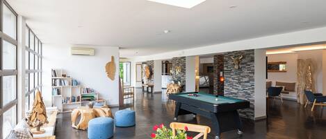 A spacious living area with a pool table, a bookshelf, and a seating area with ottomans.