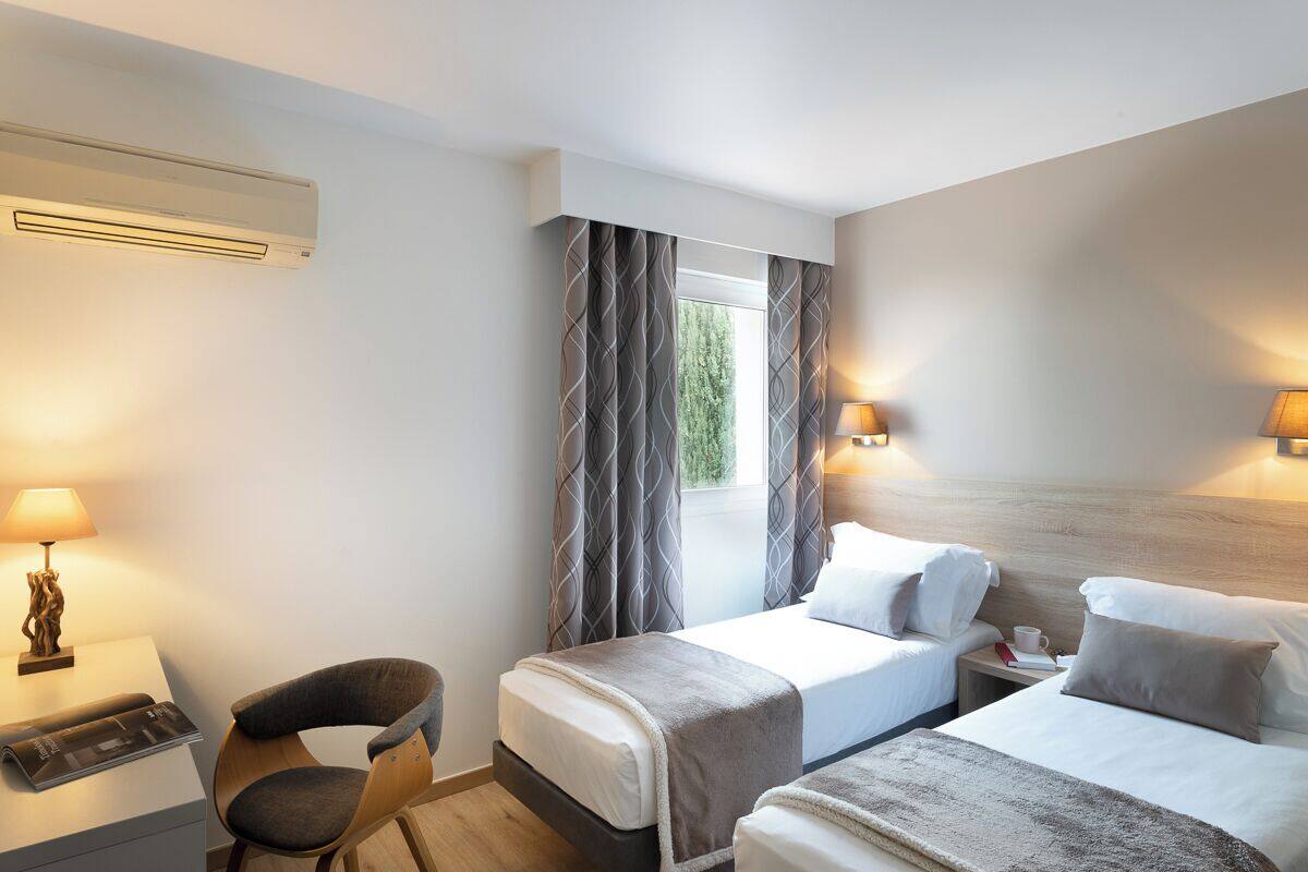 Une chambre d’hôtel avec deux lits, un bureau avec une lampe, une chaise et un appareil de climatisation.