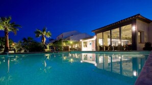 A swimming pool with a building adjacent to it, featuring large glass windows and a patio area. - Golfe Hôtel (Porto-Vecchio)